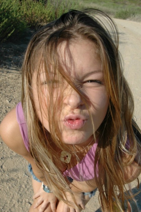 Young girl frolics on a dirt road well wearing a denim miniskirt and a thong